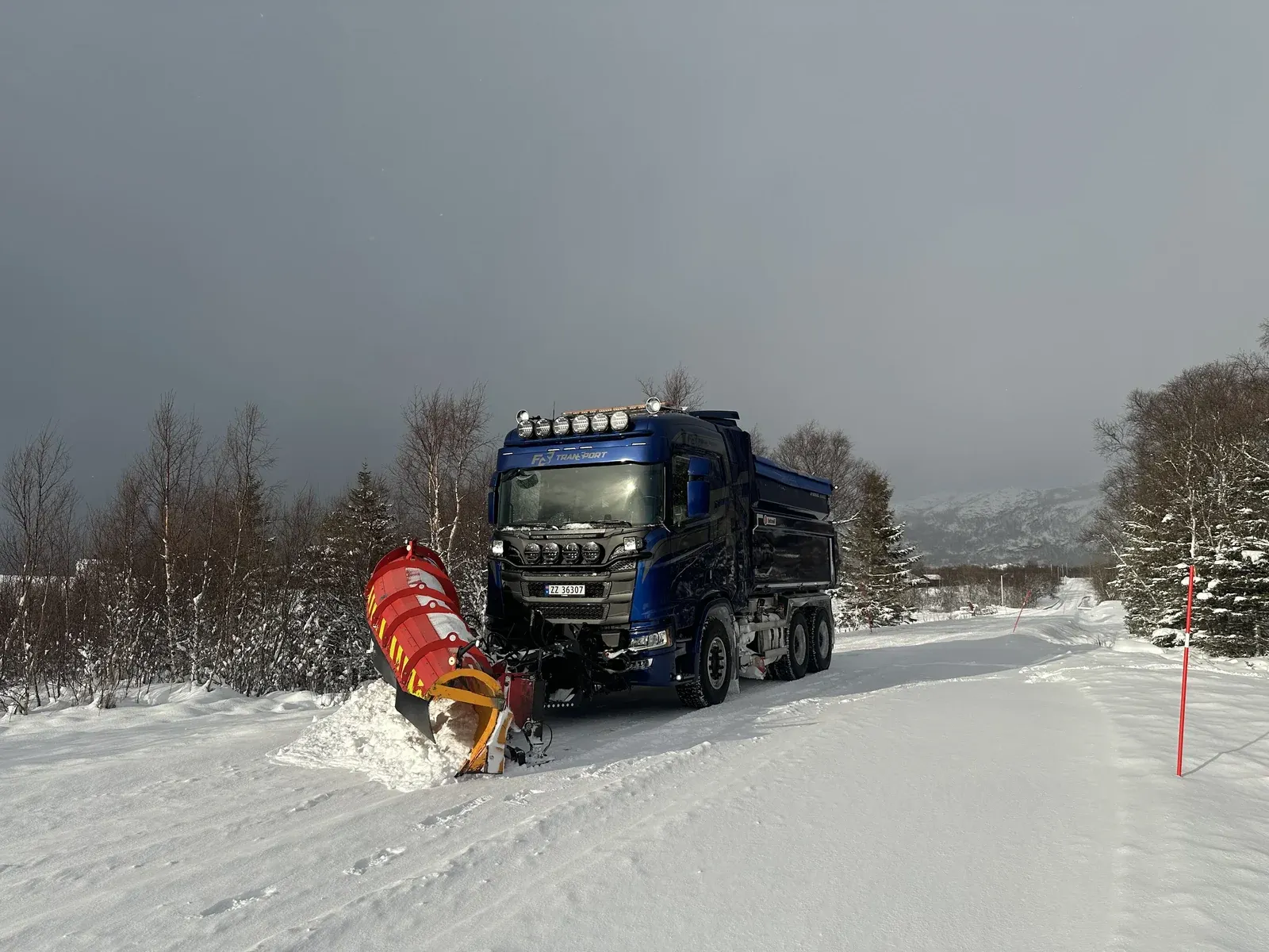Blå lastebil med rød snøplog på snødekt vei