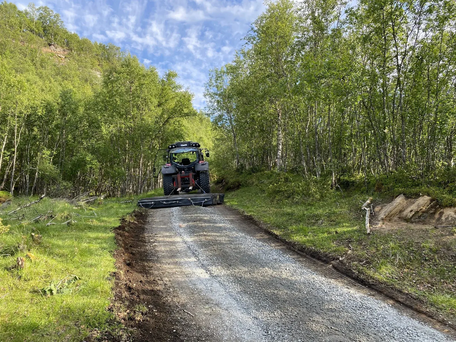Traktor som sløder en grusvei gjennom skogen