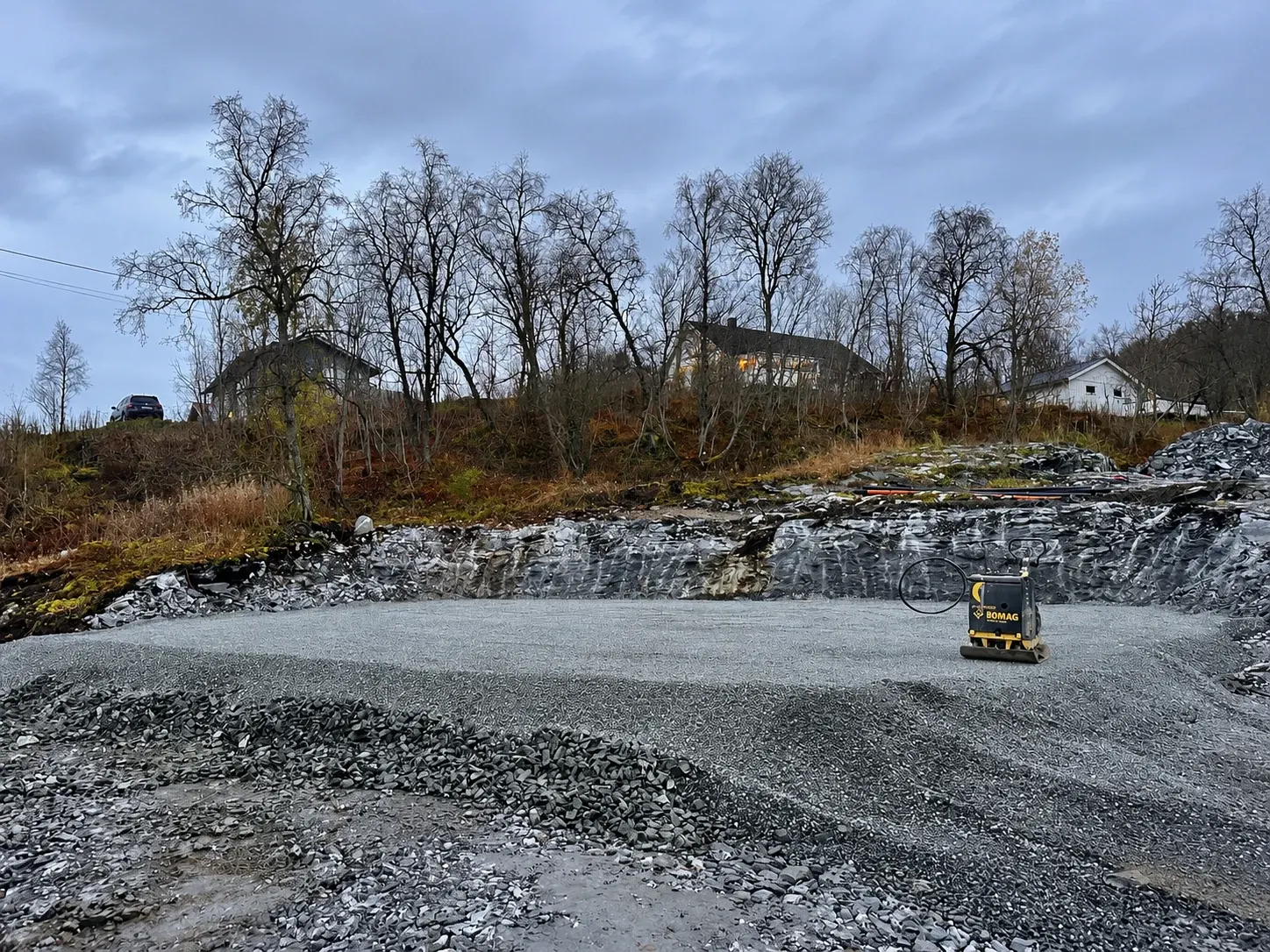 Utsprengt fjellvegg og komprimert pukk på en byggetomt med vibroplate