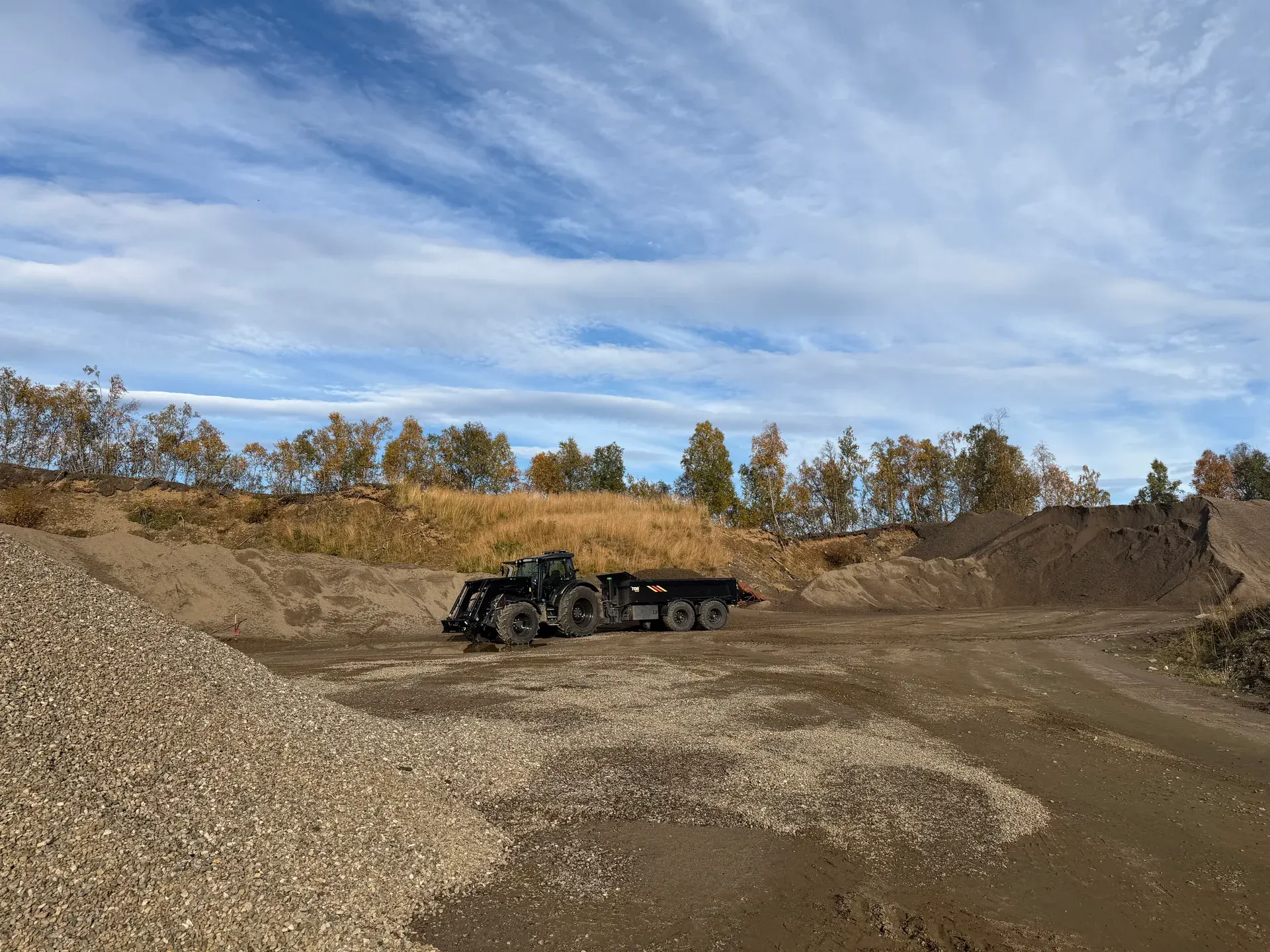 Traktor med henger mellom grus- og jordmasser