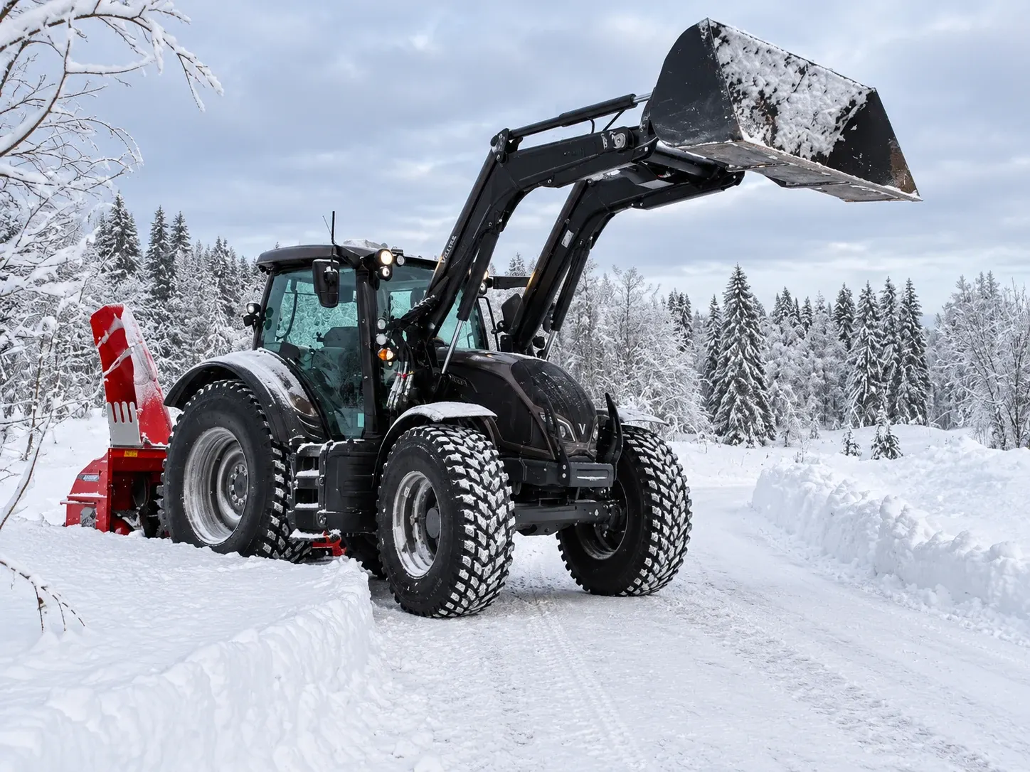 Traktor med frontlaster og snøfres på en snødekt vei i vinterlandskap