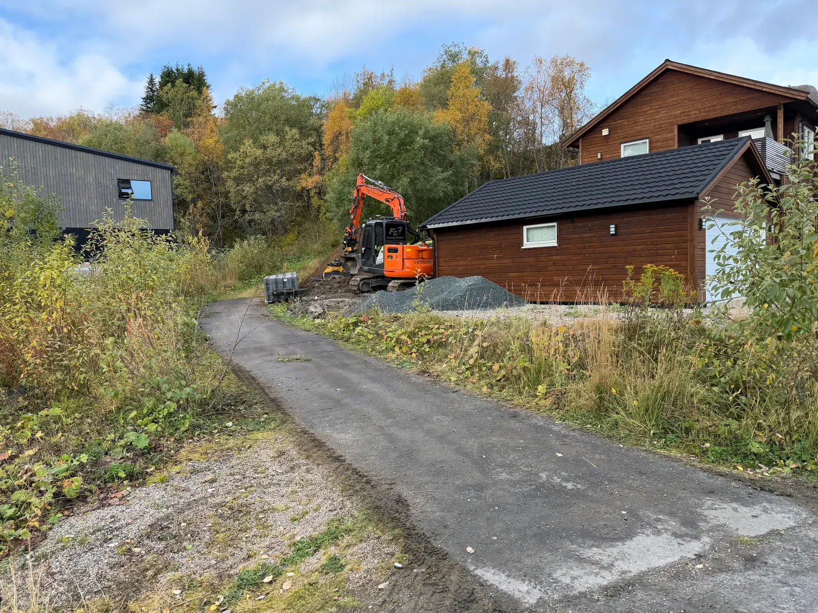 Gravemaskin ved garasje og asfaltert vei i et boligfelt
