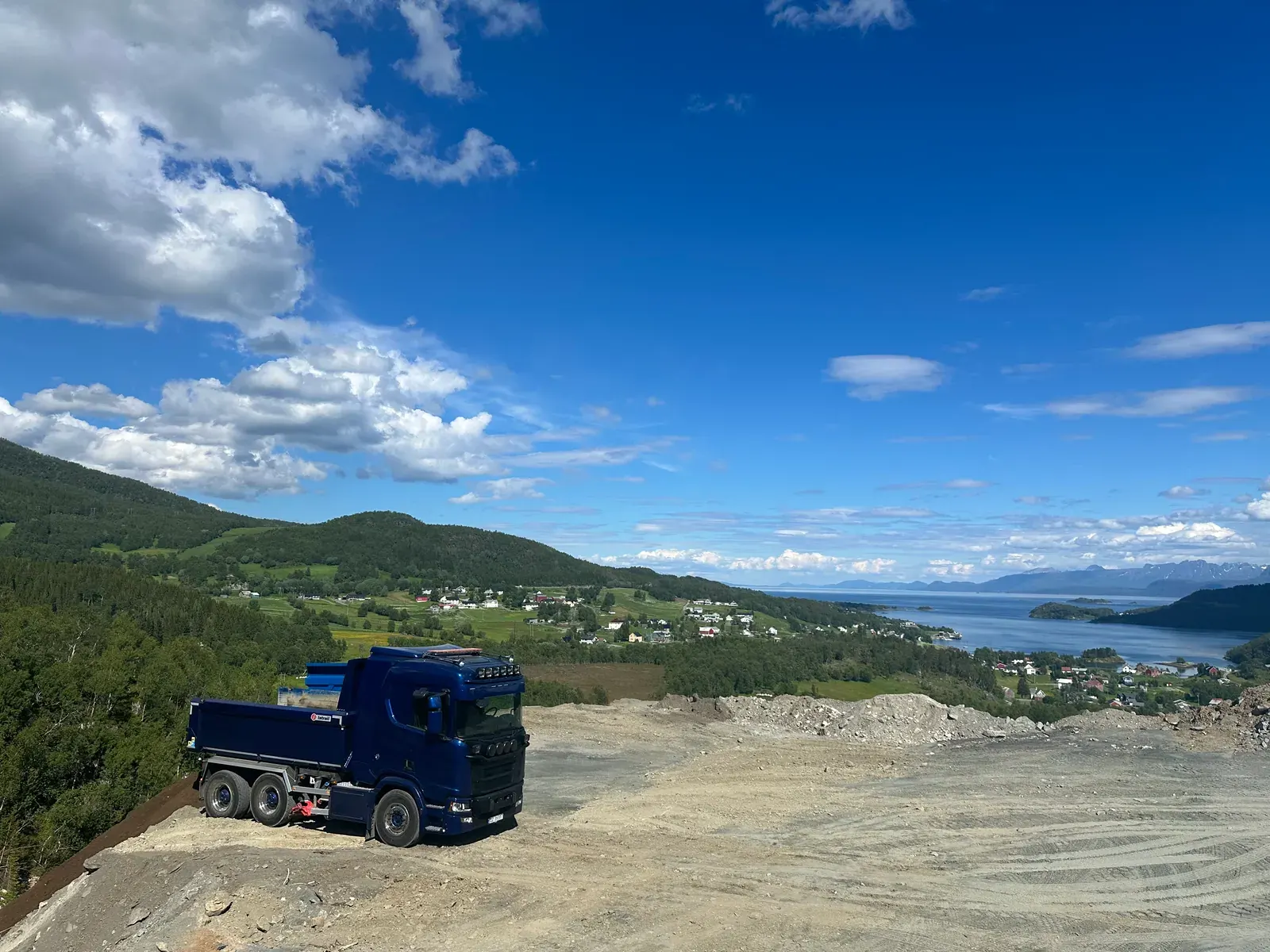 Blå tippbil på et masseuttak med utsikt over fjorden