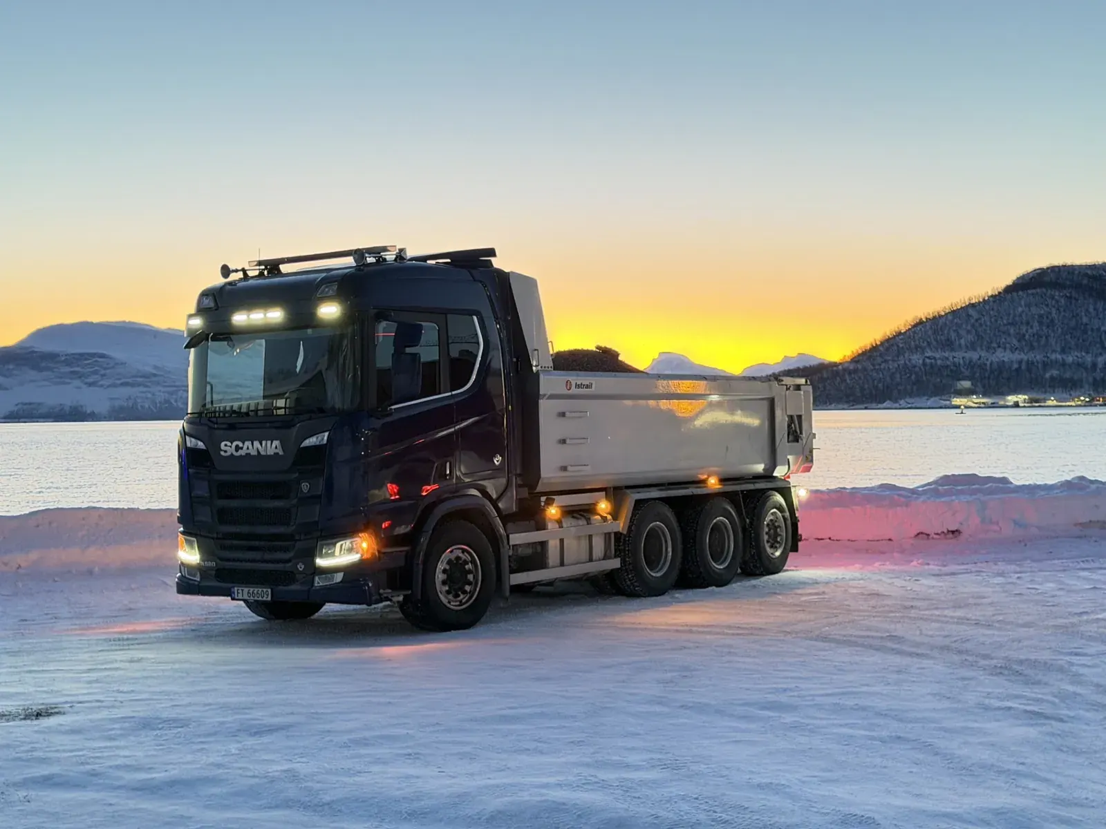 Tippbil på snødekt plass i solnedgang