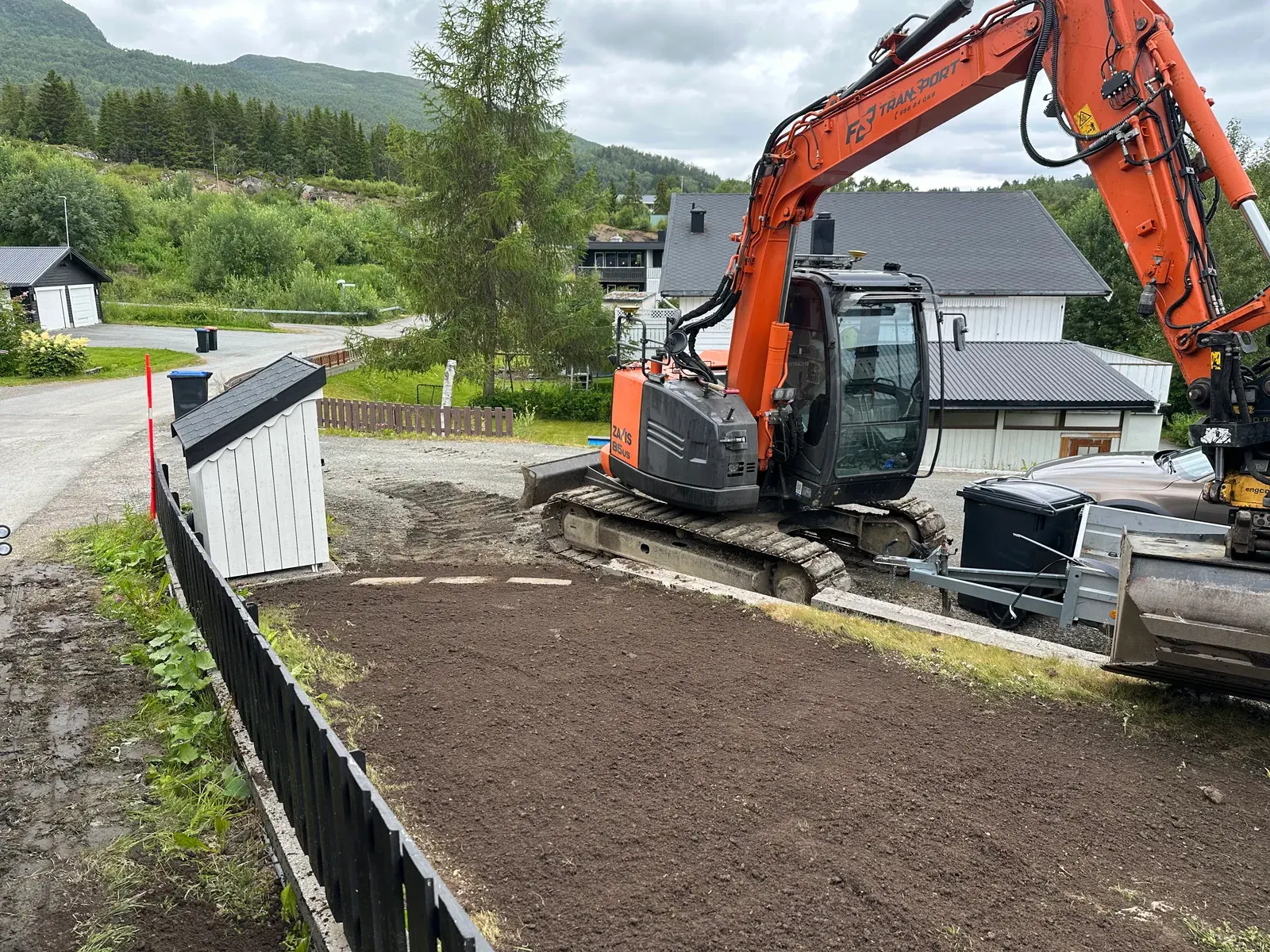Gravemaskin og ferdig tilbakefylt grøft langs et hus