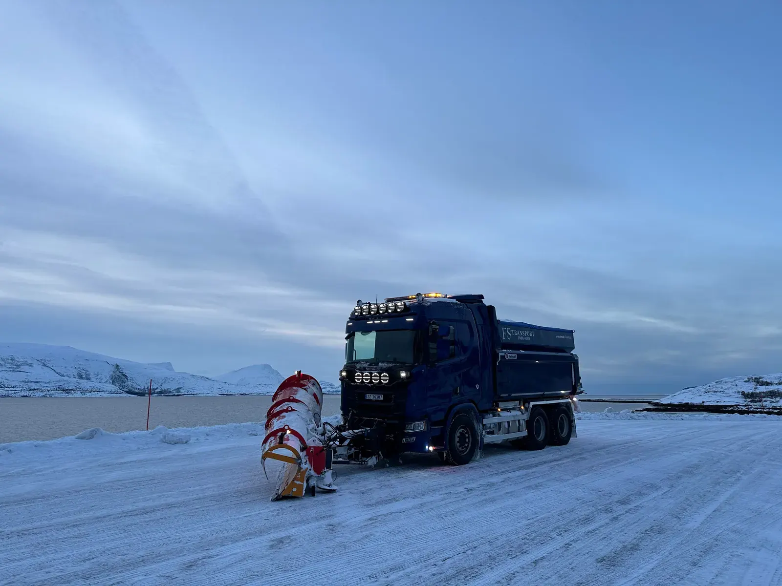 Blå brøytebil med plog på snødekt vei