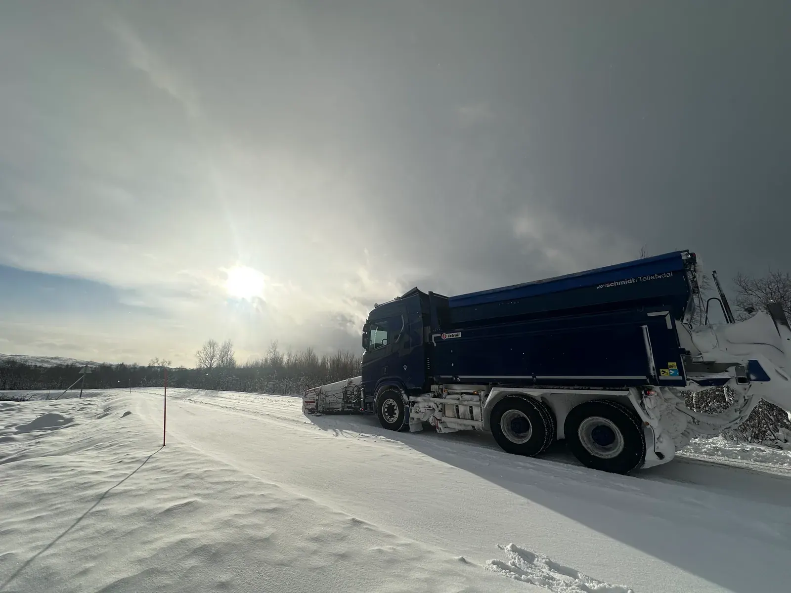 Brøytebil på snødekt vei i motlys